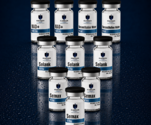 Focus and Energy | Guardian Labs Set of Guardian Labs glass vials with black caps in two staggered rows, labeled NAD+, Reconstitution Water, Selank and Semax on a dark blue speckled background (reflective surface).